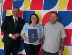 Kobieta i dwaj mężczyźni stoją obok siebie. Kobieta trzyma w ręku dokument