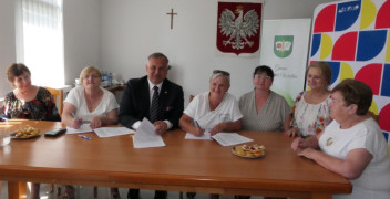 Grupa osób siedzi przy stole. Moment podpisywania umowy