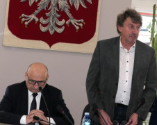 Dwaj mężczyźni za stołem prezydialnym. Jeden z nich stoi, drugi siedzi