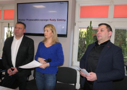 Kobieta i dwaj mężczyźni. Osoby stoją obok siebie. Kobieta w ręku trzyma białą kartkę 