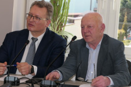 Dwaj mężczyźni siedzą obok siebie za stołem prezydialnym 