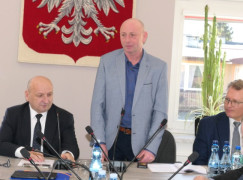 Trzech mężczyzn za stołem prezydialnym. Jeden stoi, pozostali siedzą 
