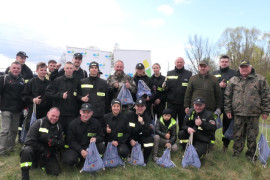 Grupa osób. Osoby stoją obok siebie. Osoby trzymają w dłoniach niebieskie worki. Uczestnicy akcji sprzątania brzegów rzeki Warty 