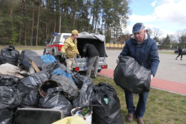 Mężczyzna niesie worek z odpadami. Dokłada go do innych worków 