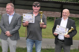 Trzej mężczyźni stoją obok siebie. Dwaj trzymają w dłoniach dyplomy i puchary