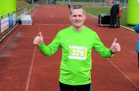 Zawodnik w zielonej koszulce stoi na bieżni z dłońmi uniesionymi w geście triumfu 
