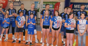 Mężczyźni - siatkarze stoją obok siebie. Przed nimi stoją dzieci