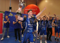 Grupa mężczyzn. Siatkarze świętują awans do II ligi. Jeden z nich trzyma w ręku puchar