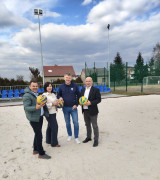 Kobieta i trzej mężczyźni stoją obok siebie na boisku do gry w piłkę siatkową. Osoby trzymają w dłoniach piłki do siatkówki 