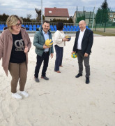 Dwie kobiety i dwaj mężczyźni stoją obok siebie. Osoby znajdują się na boisku do gry w piłkę siatkową. Kobieta i mężczyzna trzymają w dłoniach piki do siatkówki 