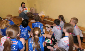Dzieci wraz z kobietą siedzą na podłodze. Trwają zajęcia edukacyjne 