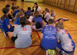 Grupa dzieci wraz z kobietą siedzi na podłodze. Trwają zajęcia edukacyjne 