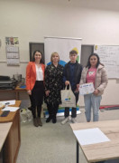 Cztery osoby pozują w klasie do zdjęcia. Chłopak trzyma torbę, kobieta dyplom