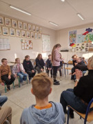 Uczniowie siedzą w kręgu i łączą sznurki w sieć, jedna dziewczynka stoi w środku sieci