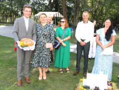 Grupa osób. Dwie z nich trzymają dożynkowy bochen chleba 