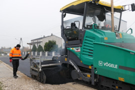 Prace podczas wylewania asfaltu. Widoczna maszyna drogowa i mężczyzna w pomarańczowej kurtce