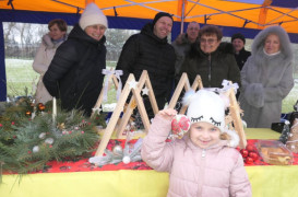 Dziewczynka trzyma w rączce bombkę. Za dziewczynką stoją dorosłe osoby
