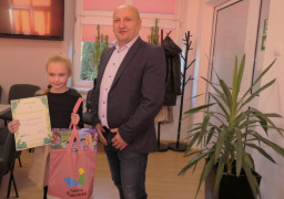 Mężczyzna i dziewczynka stoją obok siebie. Dziewczynka trzyma w ręku dyplom 