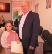 Mężczyzna i dziewczynka stoją obok siebie. Dziewczynka trzyma w ręku dyplom i torbę