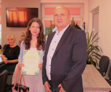 Mężczyzna i dziewczynka stoją obok siebie. Dziewczynka trzyma w ręku dyplom