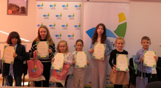 Grupa dzieci stojąca obok siebie. Dzieci trzymają w dłoniach dyplomy 