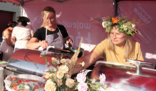 Kobieta w wianku na głowie wydaje jedzenie uczestnikom pikniku 