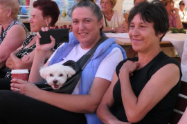 Trzy kobiety siedzą obok siebie. Jedna z nich trzyma na kolanach pieska 