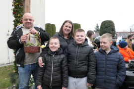 Grupa osób. Dorośli i dzieci. Mężczyzna trzyma w ręku koszyczek wielkanocny 