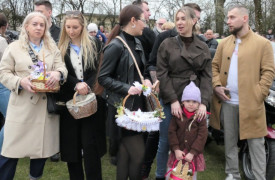 Osoby: kobiety i mężczyźni wraz z małym dzieckiem stoją na placu kościelnym. Jedna z kobiet trzyma w ręku koszyczek wielkanocny. 