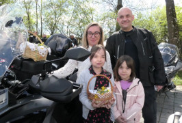 Kobieta, dwoje dzieci i mężczyzna stoją przy motocyklu, na którym znajduje się wielkanocny koszyczek