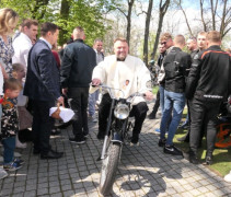 Wierni na placu kościelnym. Ksiądz jedzie na motocyklu  