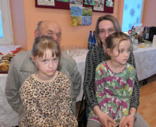 Kobieta i mężczyzna siedzą obok siebie. Na ich kolanach siedzą dziewczynki
