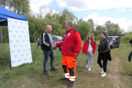 Dwaj mężczyźni podają sobie dłonie. Obok stoją dwie kobiety