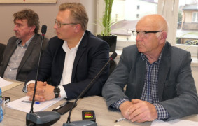 Trzej mężczyźni siedzą obok siebie. Mężczyźni przysłuchują się rozmowie 