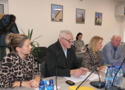 Grupa osób siedzi obok siebie. Wszyscy przysłuchują się rozmowie 