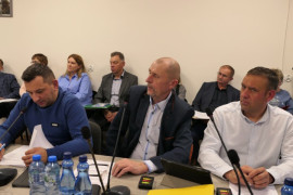 Trzej mężczyźni siedzą obok siebie. Wszyscy przysłuchują się rozmowie  