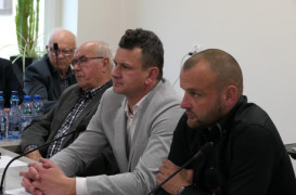 Trzej mężczyźni siedzą obok siebie. Wszyscy przysłuchują się rozmowie 