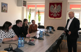Cztery osoby siedzą przy stole. Jeden mężczyzna, który przemawia stoi 