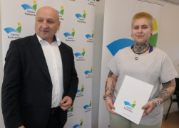 Kobieta i mężczyzna stoją obok siebie. Kobieta trzyma w ręku dyplom 