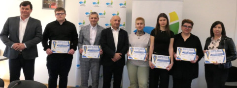 Kobiety i mężczyźni stoją obok siebie. Niektórzy z nich trzymają w ręku dyplomy