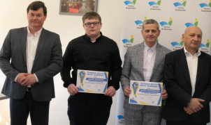 Czterej mężczyźni stoją obok siebie. Dwóch z nich trzyma w ręku dyplom 