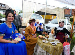 Panie w pięknych, kolorowych strojach siedzą przy stoliku podwieczorkowym przygotowanym na konkurs