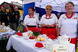 Trzy panie stoją przy stoliku podwieczorkowym 