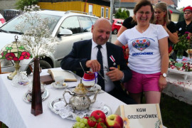 Mężczyzna siedzi na krześle znajdującym się przy stoliku podwieczorkowym, obok stoi kobieta