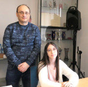 Dziewczynka siedzi przy stoliku. Obok dziewczynki stoi mężczyzna 