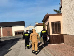 Strażacy ochotnicy idą chodnikiem wzdłuż domu