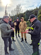Grupa mężczyzn. Strażacy wręczają mężczyźnie czujkę dymu