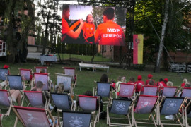 Na projektorze wyświetlany jest film. Osoby siedzą na leżakach 