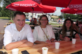 Trzy osoby siedzą przy stole. Trwa impreza plenerowa 
