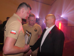Trzech panów: dwóch ubranych jest w strażackie stroje. Moment podziękowań. Panowie podają sobie dłonie
